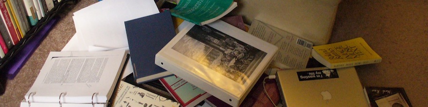 A pile of text books, ring folders, sheets of papers, and a laptop with a Creative Commons sticker