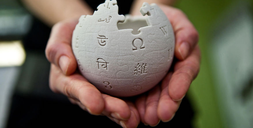 Hands are cupping a mini wikipedia globe made from wet sand