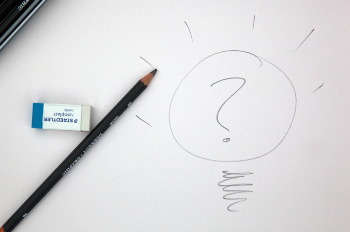 Photograph of a sketch of a question mark, alongside a pencil and an eraser