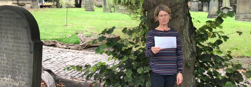 Dr Rosie Stenhouse stands in a cemetery reading a poem