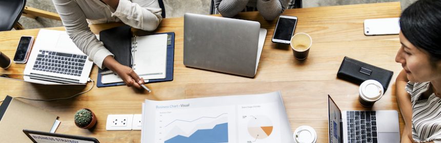 three women sitting around a table looking at graph charts and laptops