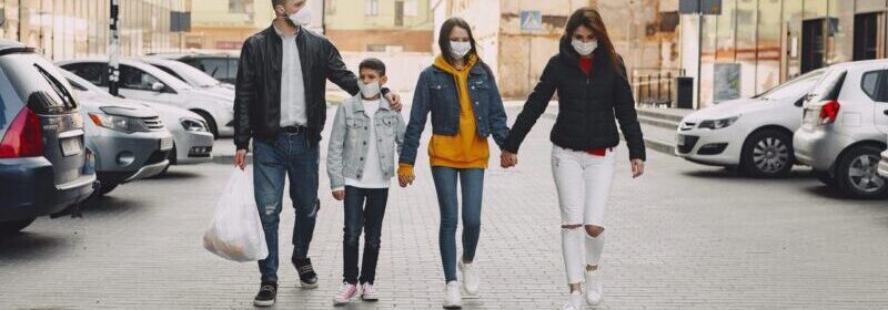 Mother, father, daughter, and son walk along a street wearing facemasks for covid protection.