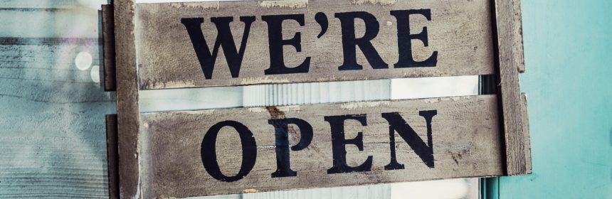 We're Open text painted on grey wood with blue background