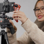 Photograph of woman wearing a headscarf and glasses, standing in front of a camera