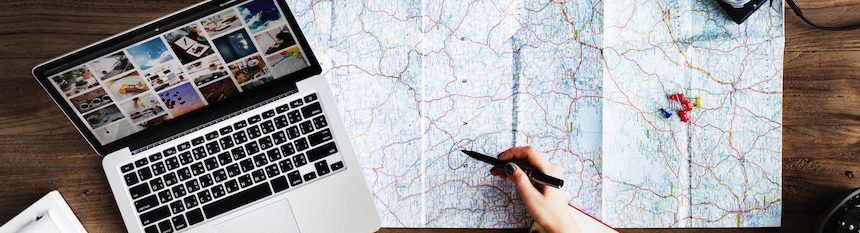 Laptop, map, and a hand holding a pen hovering over the map